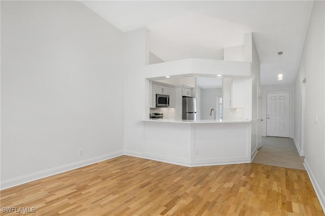 kitchen featuring kitchen peninsula, stainless steel appliances, white cabinets, light hardwood / wood-style floors, and lofted ceiling