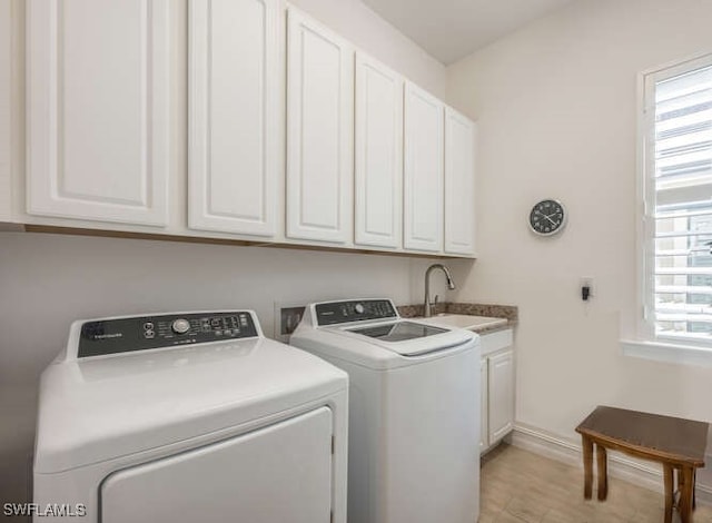 clothes washing area featuring cabinet space, light wood finished floors, baseboards, washer and clothes dryer, and a sink