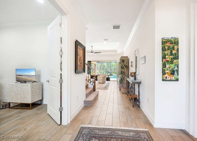 corridor featuring wood finish floors, visible vents, ornamental molding, baseboards, and stairs