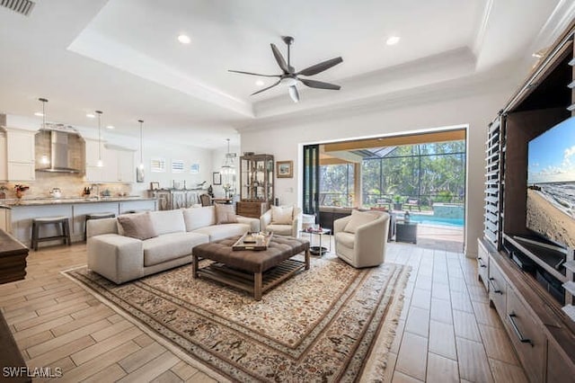 living room with wood tiled floor, a raised ceiling, visible vents, and ceiling fan