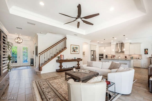 living area featuring visible vents, light wood-style flooring, stairway, a tray ceiling, and crown molding