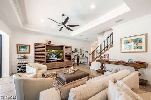 living area with stairs, a tray ceiling, light wood-style flooring, and a ceiling fan