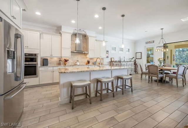 kitchen with backsplash, appliances with stainless steel finishes, white cabinetry, light stone countertops, and wall chimney exhaust hood