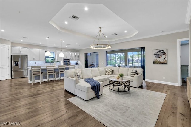 living room with crown molding, wood-type flooring, and a tray ceiling