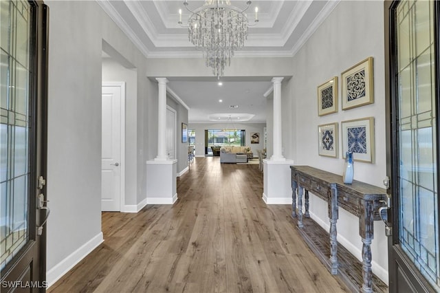 foyer entrance with a raised ceiling, a chandelier, decorative columns, light hardwood / wood-style flooring, and crown molding