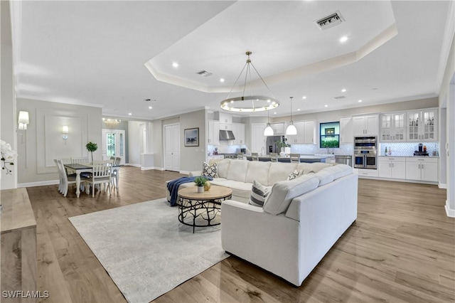 living room with light wood-type flooring, a tray ceiling, and ornamental molding