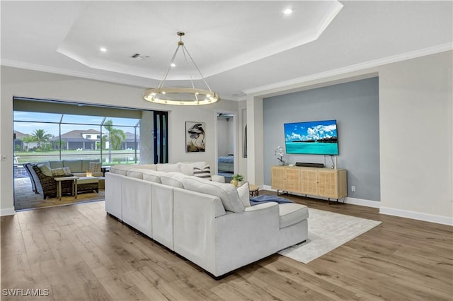 living room featuring hardwood / wood-style flooring, crown molding, and a raised ceiling