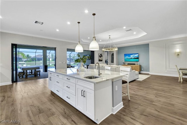 kitchen with white cabinets, decorative light fixtures, sink, a kitchen island with sink, and light stone counters