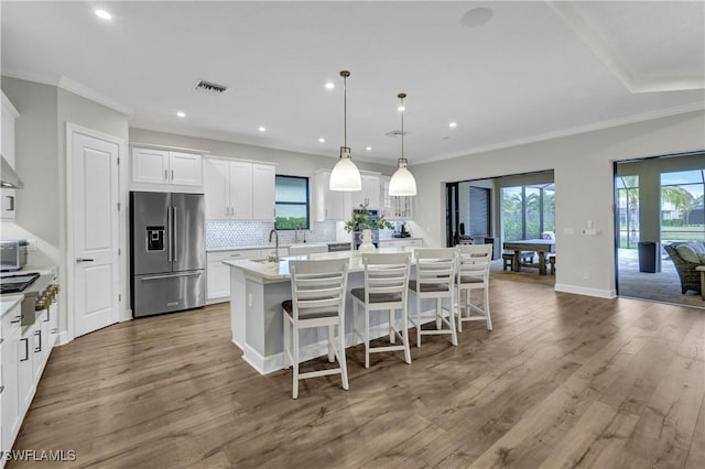 kitchen with a center island with sink, hardwood / wood-style floors, pendant lighting, stainless steel appliances, and white cabinets