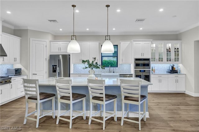 kitchen featuring a center island with sink, a kitchen bar, hanging light fixtures, stainless steel appliances, and white cabinets