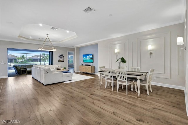 dining area featuring wood-type flooring, crown molding, and a raised ceiling