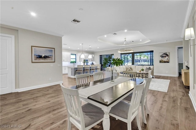 dining room featuring crown molding, light hardwood / wood-style flooring, and a raised ceiling