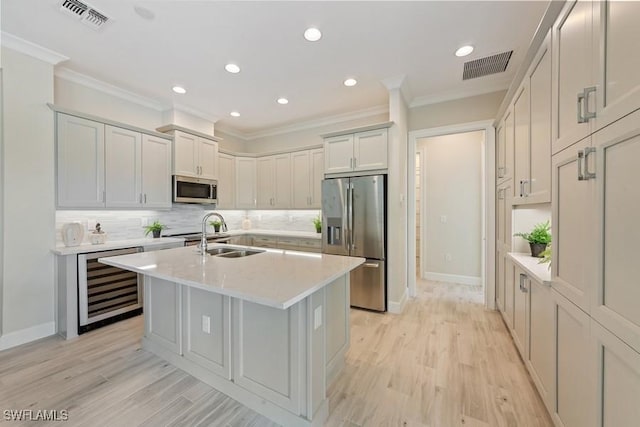 kitchen with sink, beverage cooler, stainless steel appliances, tasteful backsplash, and a center island with sink