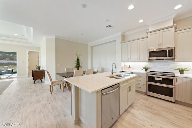 kitchen with appliances with stainless steel finishes, crown molding, sink, light hardwood / wood-style flooring, and an island with sink