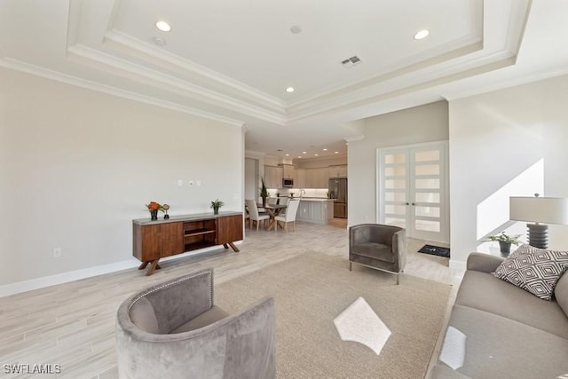 living room featuring a raised ceiling, crown molding, french doors, and light wood-type flooring