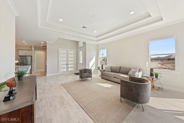 living room with a tray ceiling, french doors, ornamental molding, and light wood-type flooring