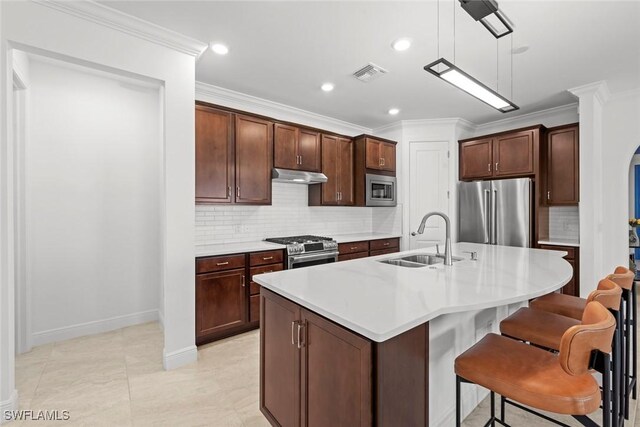 kitchen featuring stainless steel appliances, crown molding, sink, decorative light fixtures, and an island with sink