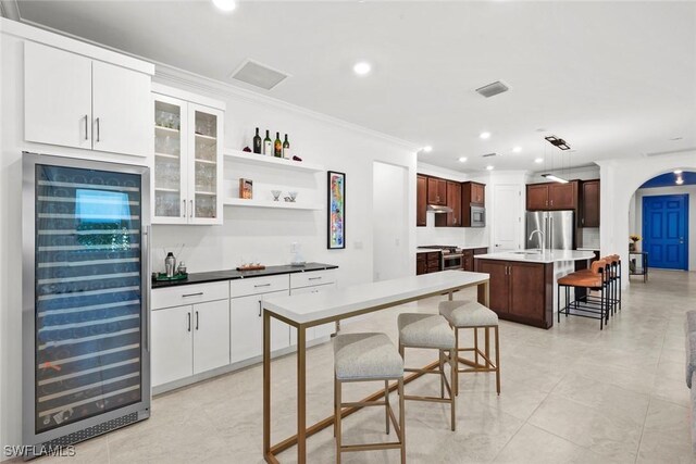 kitchen featuring beverage cooler, a breakfast bar area, a center island with sink, appliances with stainless steel finishes, and ornamental molding