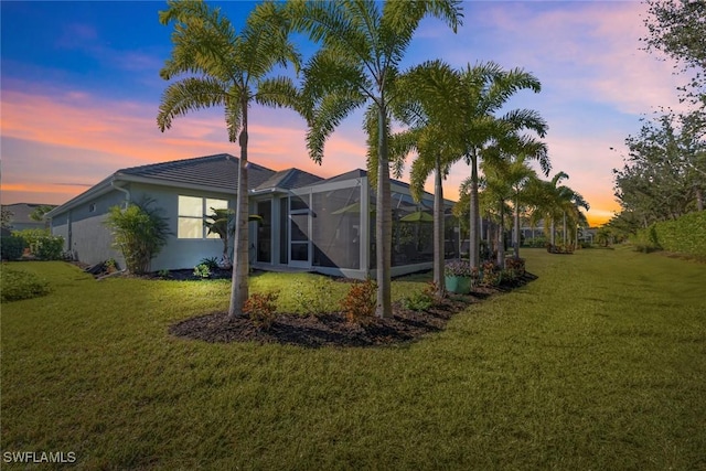 back house at dusk featuring a lanai and a lawn