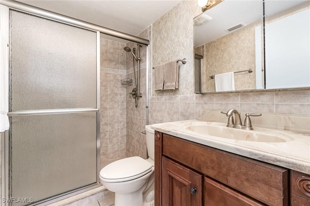 bathroom featuring vanity, a shower with door, toilet, tile walls, and tasteful backsplash