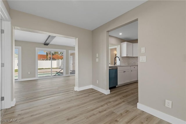 interior space featuring backsplash, white cabinets, stainless steel dishwasher, beamed ceiling, and light hardwood / wood-style floors