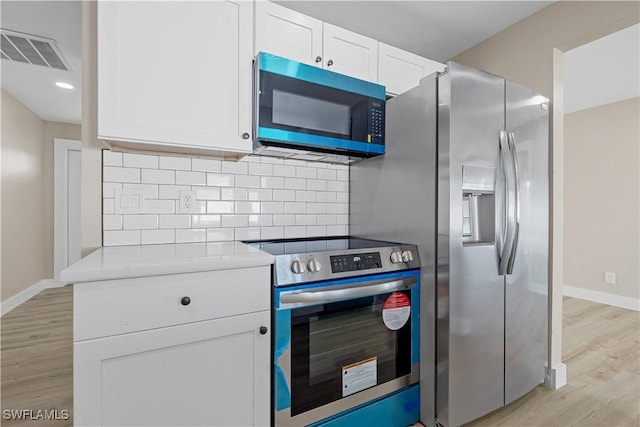 kitchen with light stone countertops, appliances with stainless steel finishes, tasteful backsplash, white cabinets, and light hardwood / wood-style floors