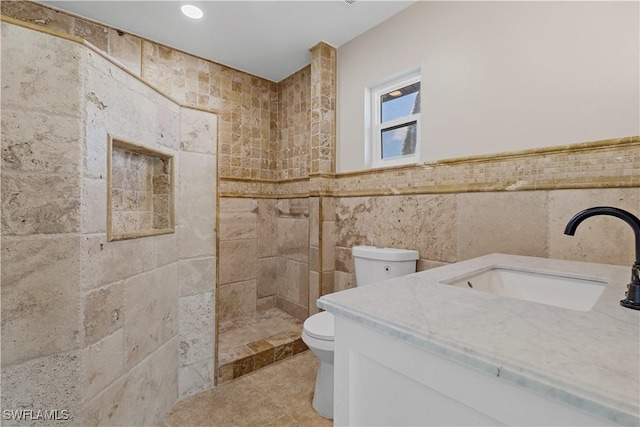 bathroom featuring vanity, toilet, tiled shower, and tile walls