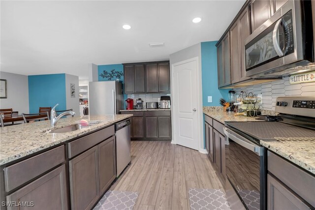 kitchen featuring light stone countertops, light wood-type flooring, sink, and appliances with stainless steel finishes