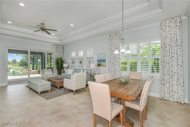 dining space with ceiling fan with notable chandelier, a raised ceiling, a healthy amount of sunlight, and crown molding