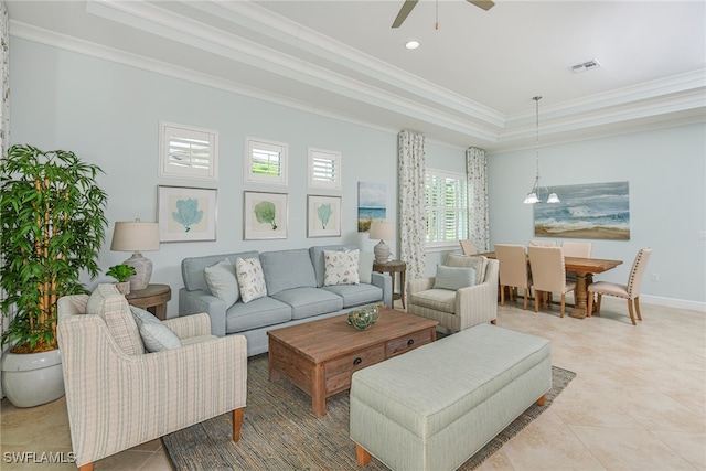 tiled living room with ceiling fan with notable chandelier, a tray ceiling, and crown molding