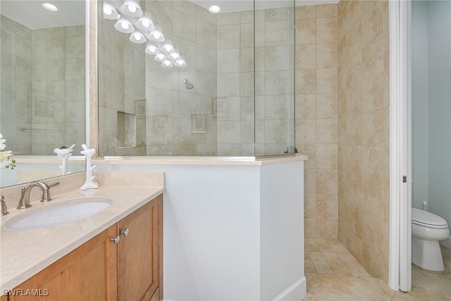 bathroom with tiled shower, tile patterned flooring, vanity, and toilet