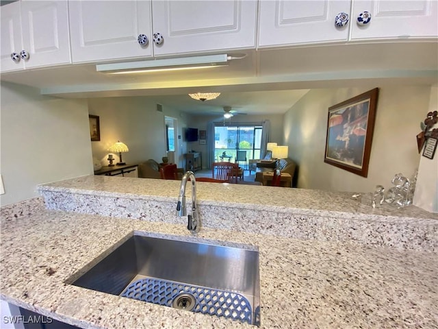 kitchen featuring white cabinetry, ceiling fan, light stone countertops, and sink