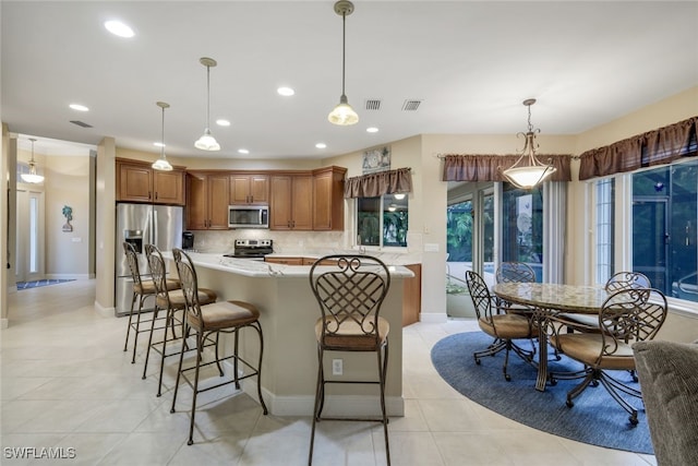 kitchen with tasteful backsplash, stainless steel appliances, decorative light fixtures, a kitchen island, and a breakfast bar area