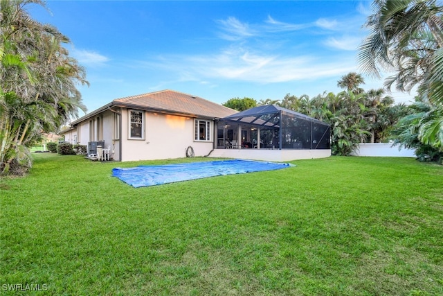 back of property with a lawn, fence, a lanai, and stucco siding