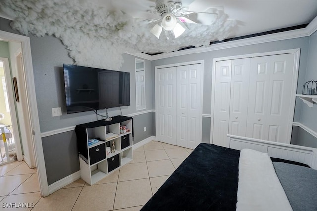 tiled bedroom with ceiling fan, crown molding, and two closets