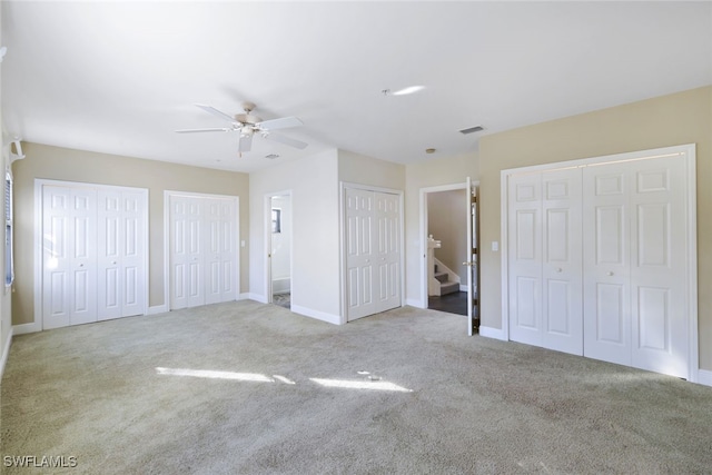 unfurnished bedroom with ceiling fan, ensuite bathroom, light carpet, and two closets