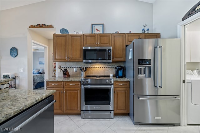 kitchen featuring light stone counters, light tile patterned floors, tasteful backsplash, washer and dryer, and appliances with stainless steel finishes