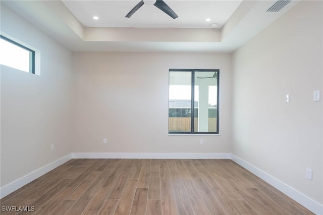 empty room with a tray ceiling, plenty of natural light, and light wood-type flooring