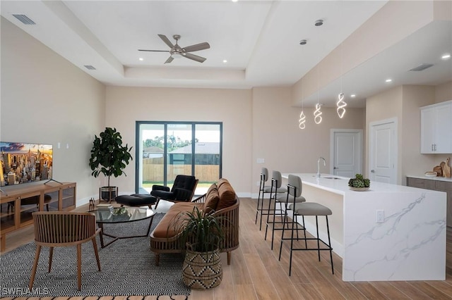 living room with ceiling fan, a raised ceiling, and sink