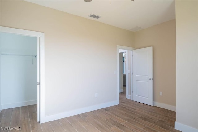 unfurnished bedroom with light wood-type flooring, a walk in closet, and a closet