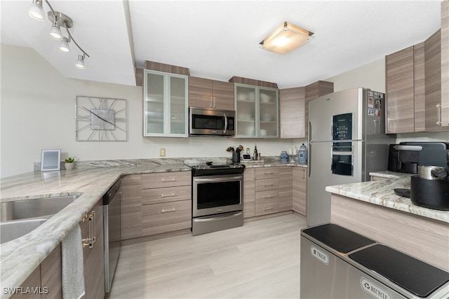 kitchen with light stone counters, glass insert cabinets, appliances with stainless steel finishes, modern cabinets, and light wood-type flooring