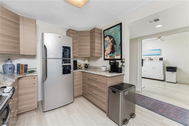 kitchen with visible vents, brown cabinetry, light stone counters, stainless steel appliances, and light wood-style floors