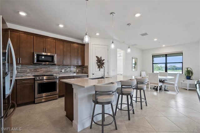 kitchen featuring appliances with stainless steel finishes, dark brown cabinetry, sink, decorative light fixtures, and a center island with sink