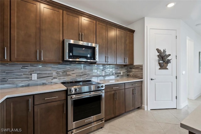 kitchen with dark brown cabinetry, light tile patterned floors, backsplash, and appliances with stainless steel finishes