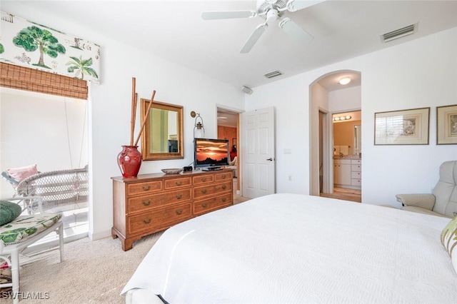 bedroom with light colored carpet, arched walkways, visible vents, and connected bathroom