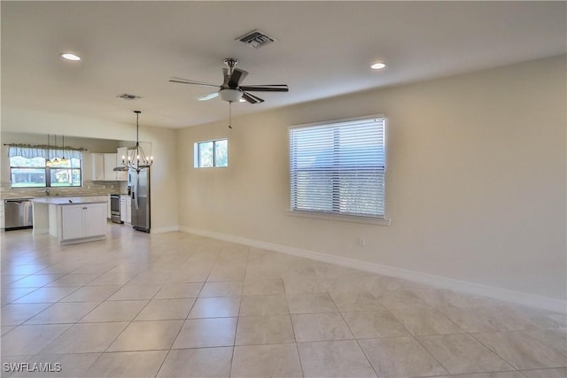 empty room with ceiling fan with notable chandelier, light tile patterned flooring, and a healthy amount of sunlight