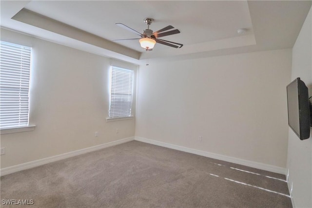 empty room with a raised ceiling, ceiling fan, and carpet