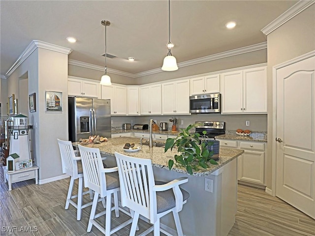 kitchen with light stone countertops, white cabinetry, stainless steel appliances, and a kitchen island with sink