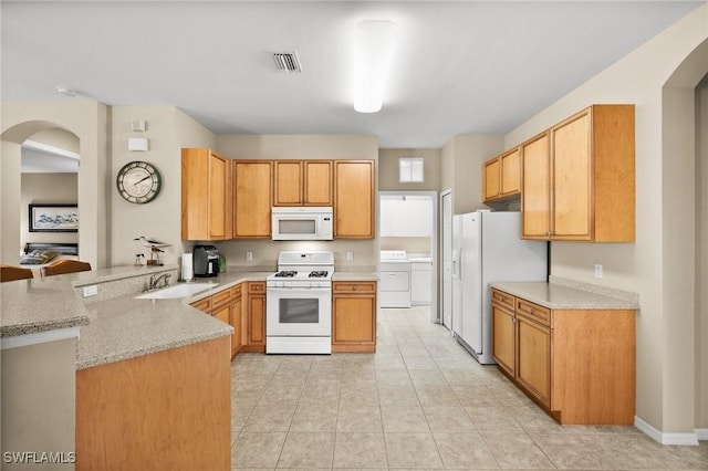 kitchen with kitchen peninsula, light stone counters, sink, and white appliances