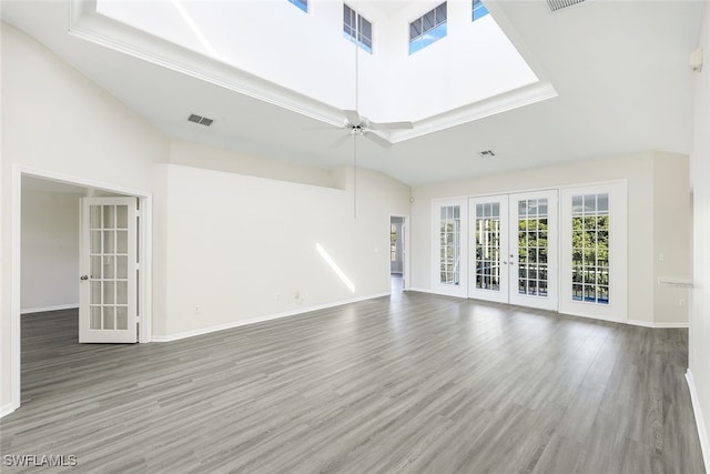 unfurnished living room featuring a towering ceiling, french doors, hardwood / wood-style flooring, ceiling fan, and a tray ceiling